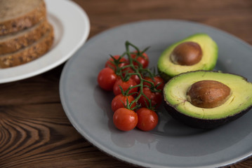 Preparing and cooking healthy avocado sandwich on dark rye toast bread made with fresh avocado paste, cherry tomatoes on brown wooden background