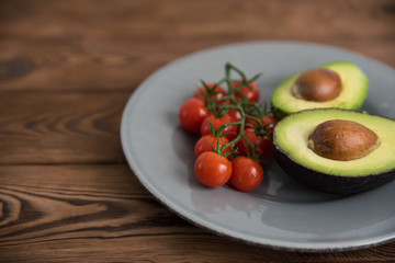 Healthy fresh avocado and cherry tomatoes on the plate on brown wooden background