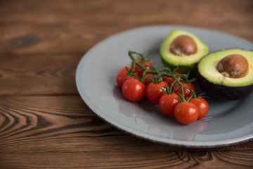 Healthy fresh avocado and cherry tomatoes on the plate on brown wooden background