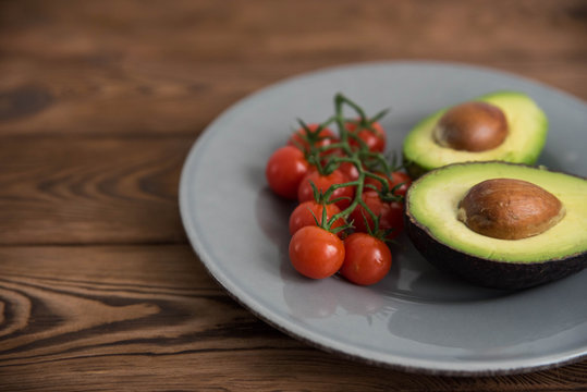 Healthy fresh avocado and cherry tomatoes on the plate on brown wooden background - Powered by Adobe