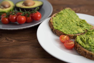 Healthy avocado sandwich on dark rye toast bread made with fresh avocado paste, cherry tomatoes on brown wooden background