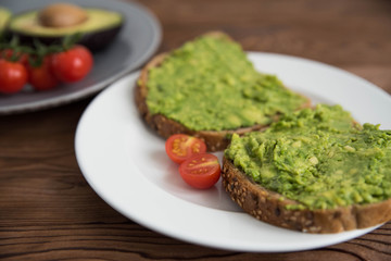 Healthy avocado sandwich on dark rye toast bread made with fresh avocado paste, cherry tomatoes on...