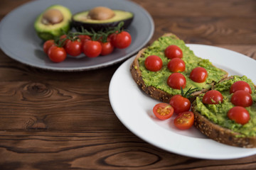 Healthy avocado sandwich on dark rye toast bread made with fresh avocado paste, cherry tomatoes on...