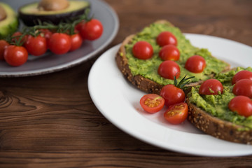 Healthy avocado sandwich on dark rye toast bread made with fresh avocado paste, cherry tomatoes on brown wooden background