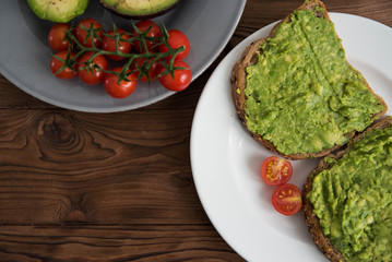 Healthy avocado sandwich on dark rye toast bread made with fresh avocado paste, cherry tomatoes on brown wooden background