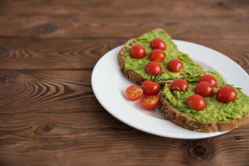 Healthy avocado sandwich on dark rye toast bread made with fresh avocado paste, cherry tomatoes on brown wooden background