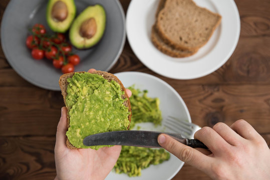 Hands of cook chef preparing healthy avocado sandwich on dark rye toast bread made with fresh avocado paste, cherry tomatoes on brown wooden background - Powered by Adobe