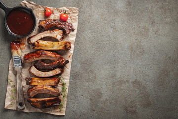 Closeup of pork ribs grilled with BBQ sauce and caramelized in honey. Tasty snack to beer on a paper for filing on dark concrete background. Top view with copy space. Flat lay - obrazy, fototapety, plakaty