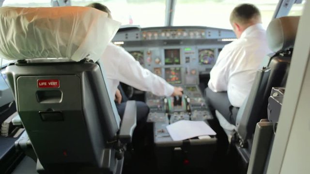 Two airplane pilots inside the cockpit are checking the instruments and preparing for take-off 