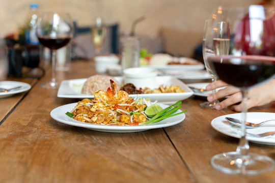 Famous Pad Thai noodles with shrimps and glass of red wine on wooden table.