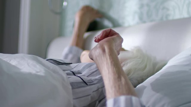 Lock down of old woman discontentedly turning off alarm clock and continuing sleep in the morning