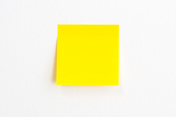 Yellow post it paper note on a white wall background with empty space.