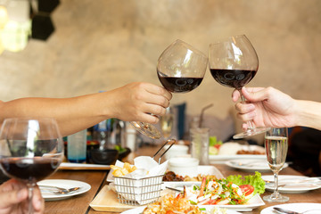 Friends celebration lunch with hands toasting glass red wine with food.