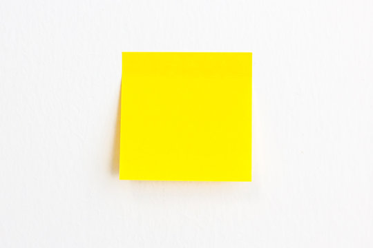Yellow post it paper note on a white wall background with empty space.