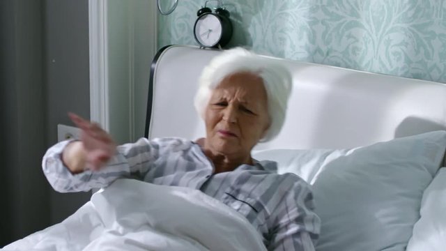 Tilt up of old woman discontentedly turning off alarm clock and continuing sleep in the morning