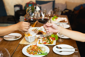 Friends celebration lunch with hands toasting glass red wine with food.