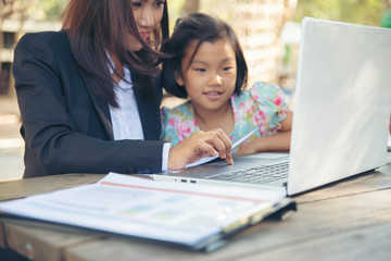 Asian Mother is teaching homework to dauther with laptop.Businesswoman and kid playing computer games together at home.Happy family Concept.