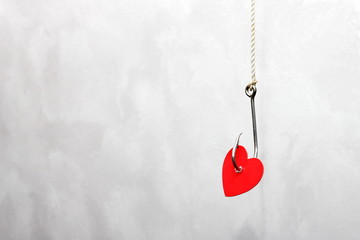 A metal fishing hook hanging on a rope pierced the Red cardboard heart. Сoncept of love. Valentines day