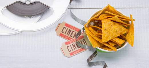 a bucket of nachos on a light background, two movie tickets and film stock