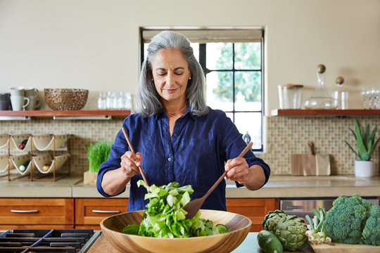 Mature woman tossing a healthy salad in the kitchen at home 