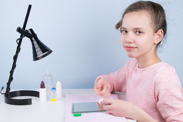 the girl sits at the table and puts on a contact lens to improve vision