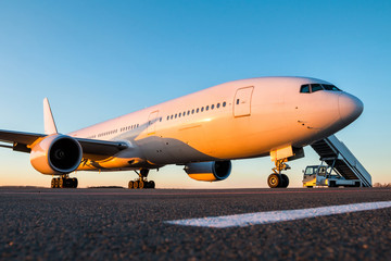 White wide-body passenger aircraft with air-stairs at the airport apron in the evening sun