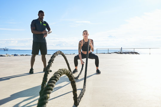 Sportswoman doing exercise with ropes with personal trainer.