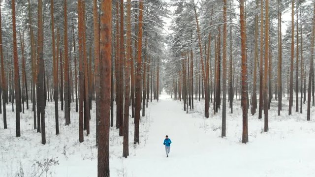 Winter Sports And Active Lifestyle Concept: Young Teen Man Running Outdoor Winter Forest Trail. Jogging In Winter. Male Runner in Park. Fitness and Wellness Concept. Healthy Lifestyle