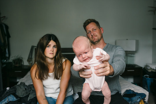 Stressed and tired new parents with screaming newborn baby on bed