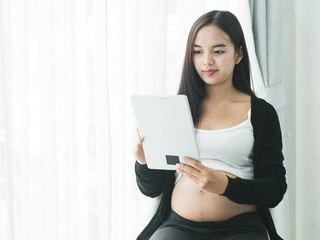 Asian pregnant woman using tablet on bed at home, lifestyle concept.