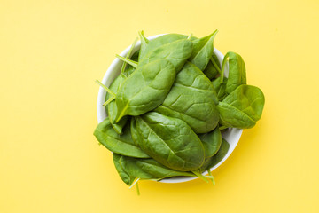 Fresh spinach leaves in a plate on a yellow background.