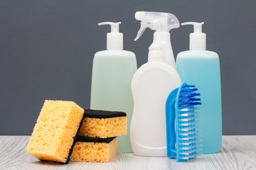 Bottles of dishwashing liquid, brush and sponges on gray background.