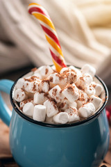 Mug of hot chocolate with marshmallow and a Lollipop stick on a knitted blanket background. Cozy warm winter composition