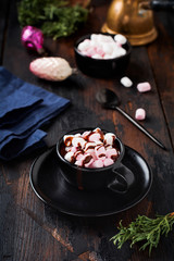 Hot chocolate with marshmallow candies in black ceramic cup on old dark vintage wooden background. Selective focus.