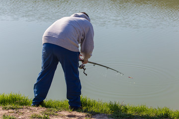 A man with a fishing rod is fishing on the river bank