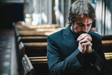 Lonely Christian man praying in the church - obrazy, fototapety, plakaty