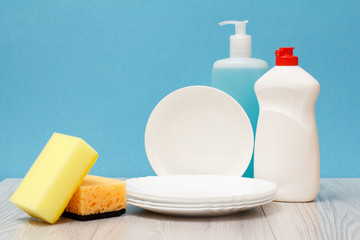 Bottles of dishwashing liquid, plates and sponges on blue background.