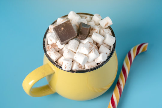 Mug of hot chocolate with marshmallows on top and stick a Lollipop on a blue background. Cozy winter card