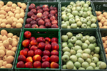 A large rack with baskets with different types of apples in the fruit department of the shopping center. Fresh and healthy foods for the diet on a daily basis among which bright red apples stand out