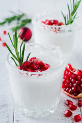 Christmas coconut punch with pomegranate seeds and sprigs of rosemary on light background. Selective fоcusе. Top view.