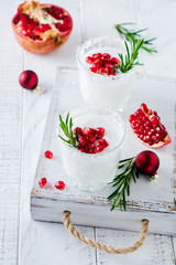 Christmas coconut punch with pomegranate seeds and sprigs of rosemary on light background. Selective fоcusе. Top view.