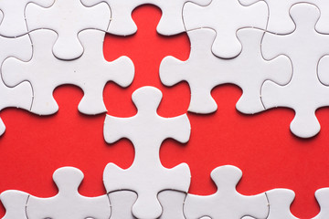 Unfinished white jigsaw puzzle pieces on red background