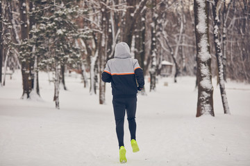 Man jogging in a cold winter snowy day outdoors.