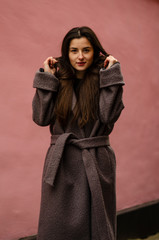 Fashion portrait of pretty brunette smiling hipster woman in a gray coat against the pink wall. Fashionable young woman posing outside in a city street. Winter Fashion