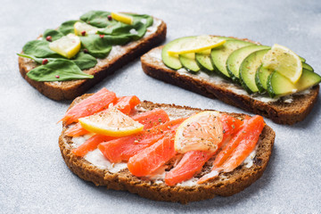 Open sandwiches with spinach and avocado salmon on a grey table.