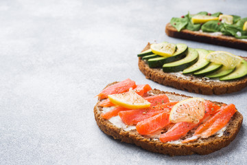 Open sandwiches with spinach and avocado salmon on a grey table. Copy space