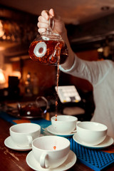 A transparent cup of black tea, a teapot and mint on a mirror table at a dark background