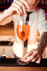 Barman hands decorating a glass of fresh and tasty Aperol syringe cocktail with red rose petals