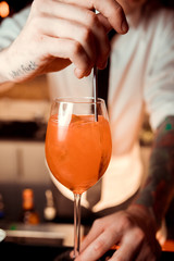Barman hands decorating a glass of fresh and tasty Aperol syringe cocktail with red rose petals