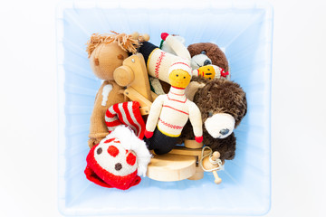 Top view of funny vintage children toys in a blue plastic box on white background. Assortment consists of a clown, a squirrel, a teddy bear, dolls, a wooden grasshopper and a ball.